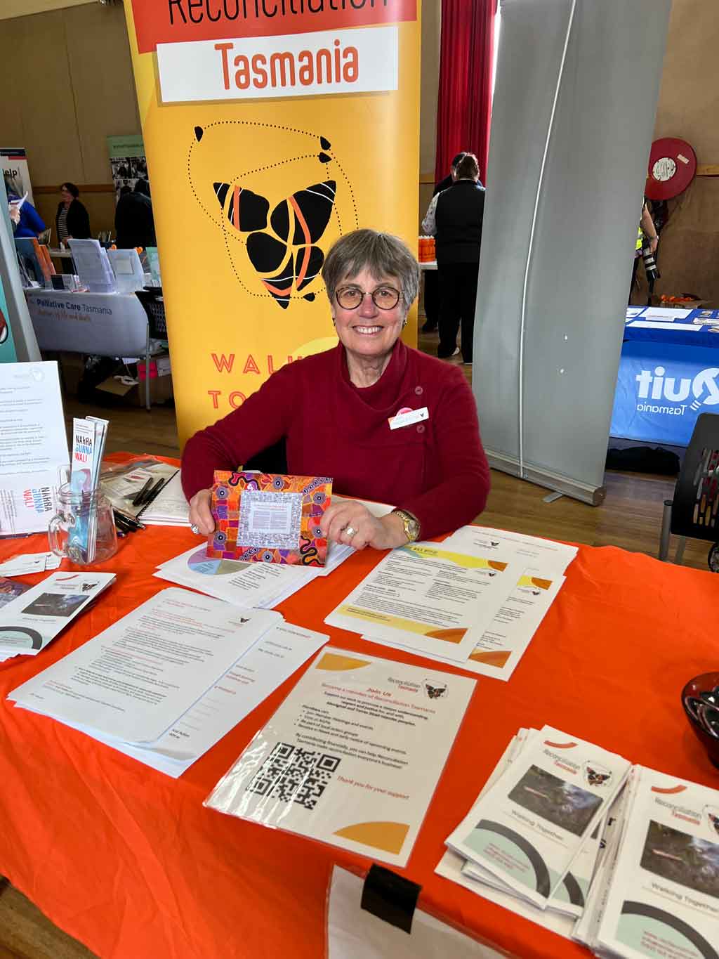 A photo of a woman sitting at a Reconciliation Tasmania information table